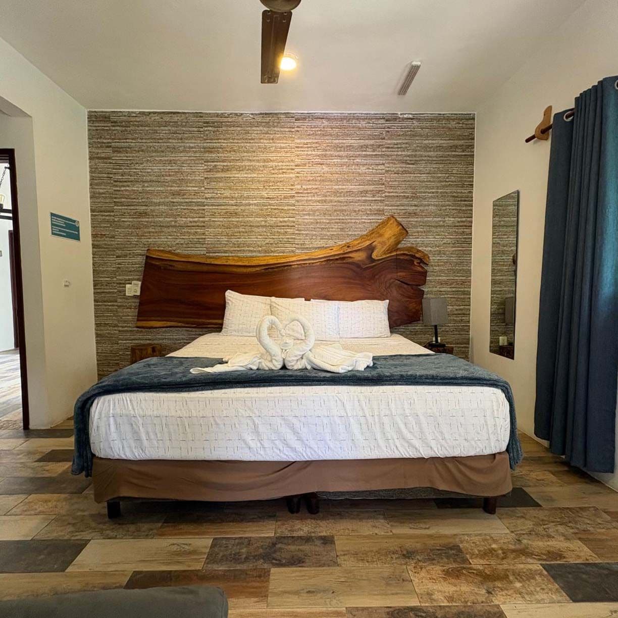 Een hotelkamer met een groot bed, een houten hoofdbord, een structuurwand en een spiegel.