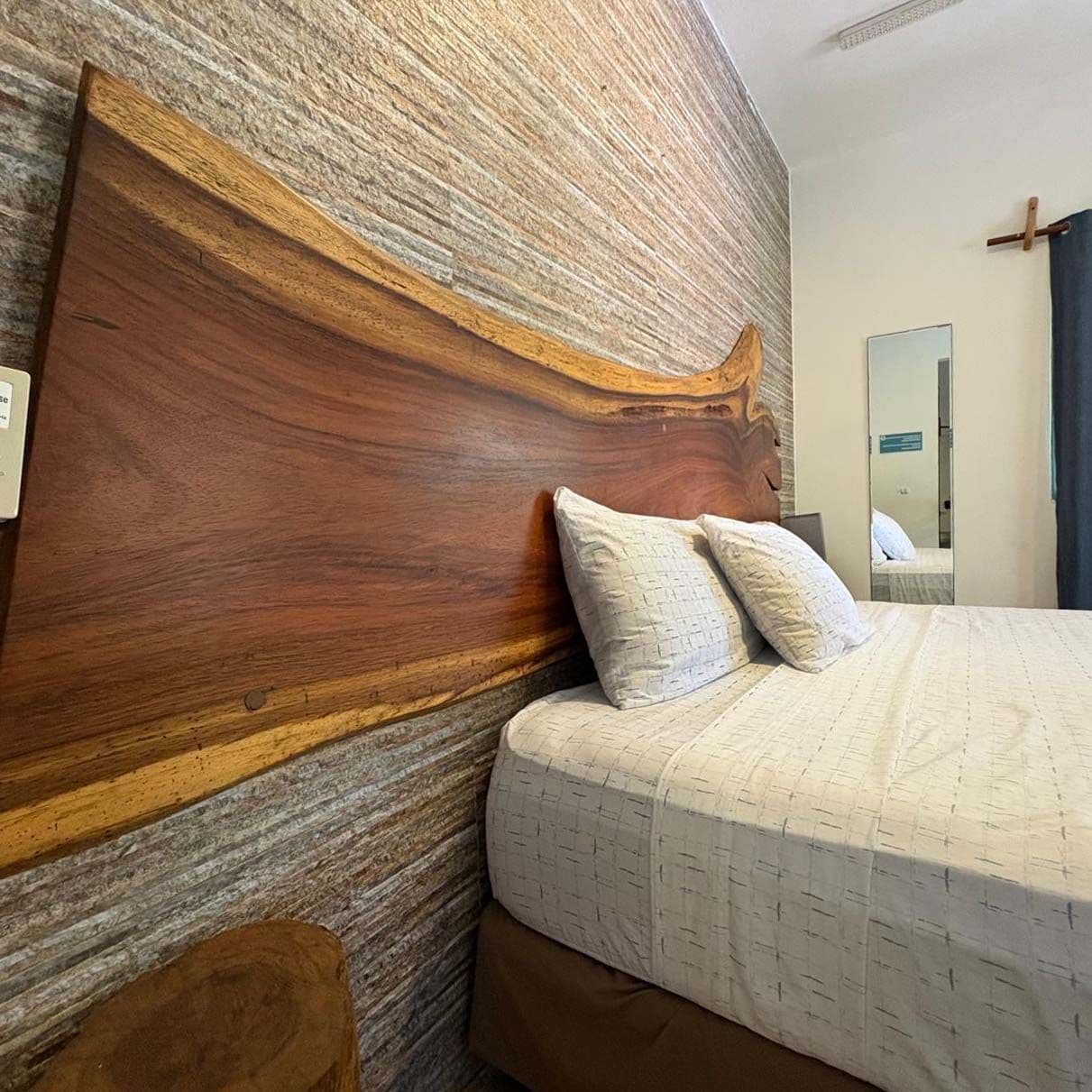 Een hotelkamer met een groot houten hoofdeinde, een bed met witte lakens en een spiegel aan de muur.