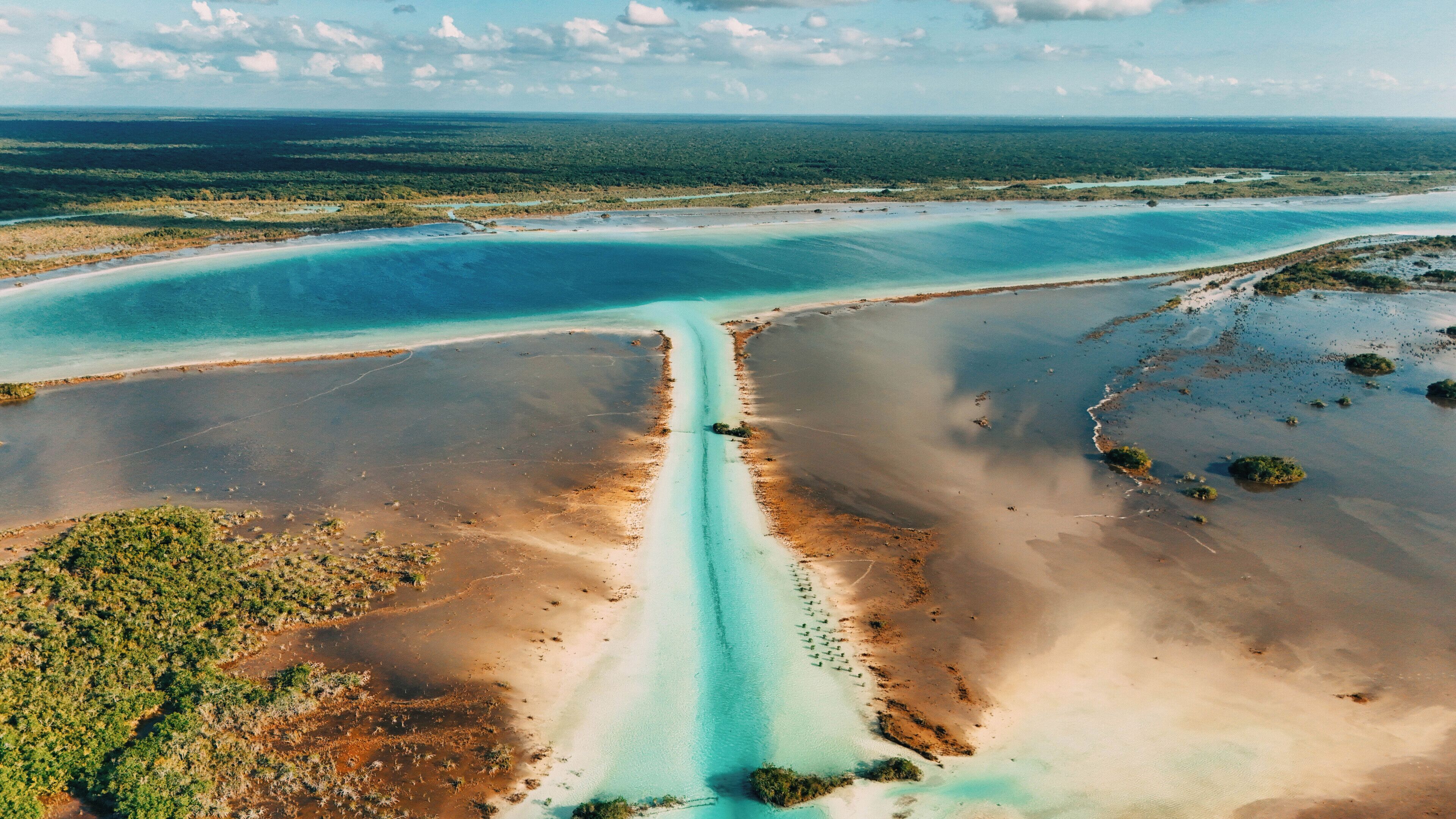 Vue aérienne d’un paysage côtier comprenant un étroit canal d’eau, des zones sablonneuses et une végétation dense.
