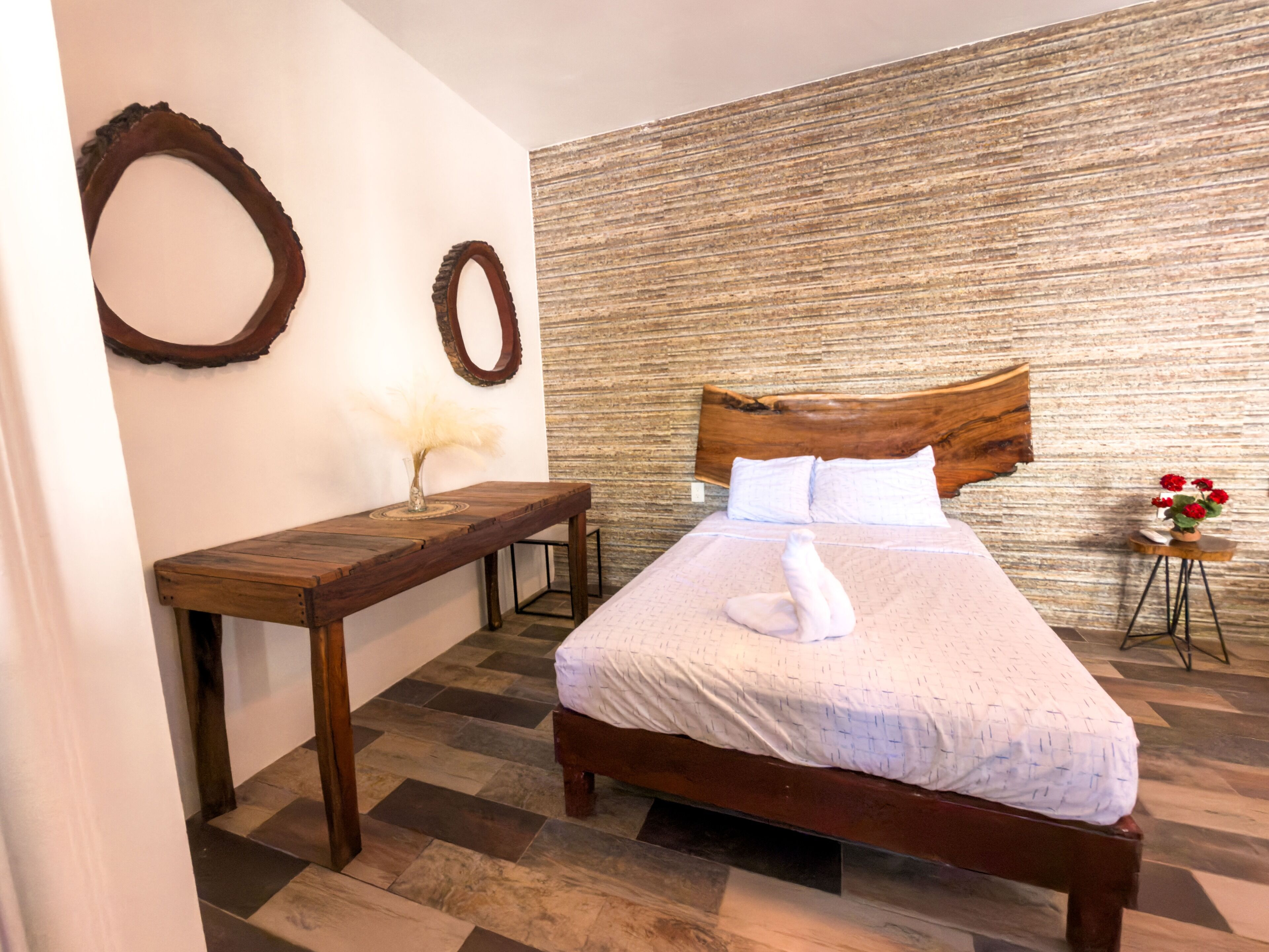 Un dormitorio ordenado con una cama de madera, una mesita pequeña y un espejo montado en la pared.