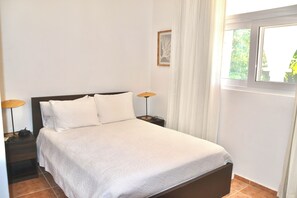 A neatly made bed with a white bedspread, two bedside lamps, and a window with curtains. - Oceanview Hideaway Apartment, Steps from the Beach (Cabarete)