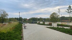 A paved walkway with benches, surrounded by greenery and a body of water. - Comfortable apartment, SPA zone, Dziwnow (Dziwnów)