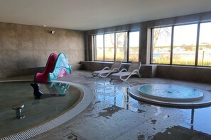An indoor swimming pool area with a hot tub, lounge chairs, and a colorful children's play structure. - Comfortable apartment, SPA zone, Dziwnow (Dziwnów)