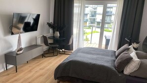 A modern bedroom with a bed, a desk, a chair, a TV, and a balcony with a view. - Comfortable apartment, SPA zone, Dziwnow (Dziwnów)