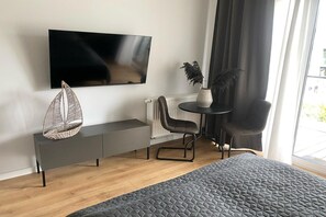 Moderni hotellihuone, jossa on sänky, seinälle asennettu televisio, pieni pöytä tuoleineen ja ikkuna, jossa on verhot.