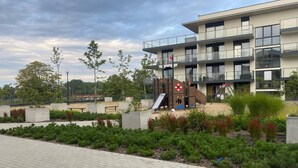 A modern building with a playground, including a slide and climbing structures, surrounded by landscaped areas with shrubs and trees. - Comfortable apartment, SPA zone, Dziwnow (Dziwnów)
