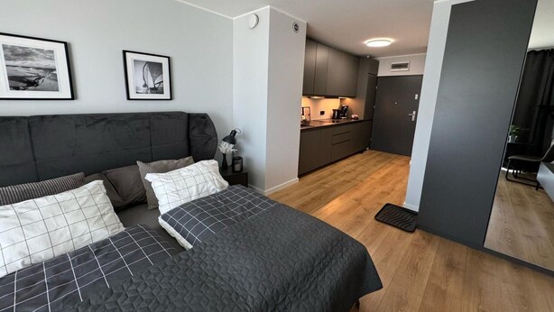 A modern bedroom with a large bed, a bedside table, and a small kitchen area with cabinets and a sink. - Comfortable apartment, SPA zone, Dziwnow (Dziwnów)