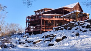 A multi-story wooden cabin with a balcony, situated on a snow-covered slope. - Cozy 2-bedroom rustic cabin in Red River Gorge area,Hot Tub, Pilots Knob Hiking (CLAY CITY)
