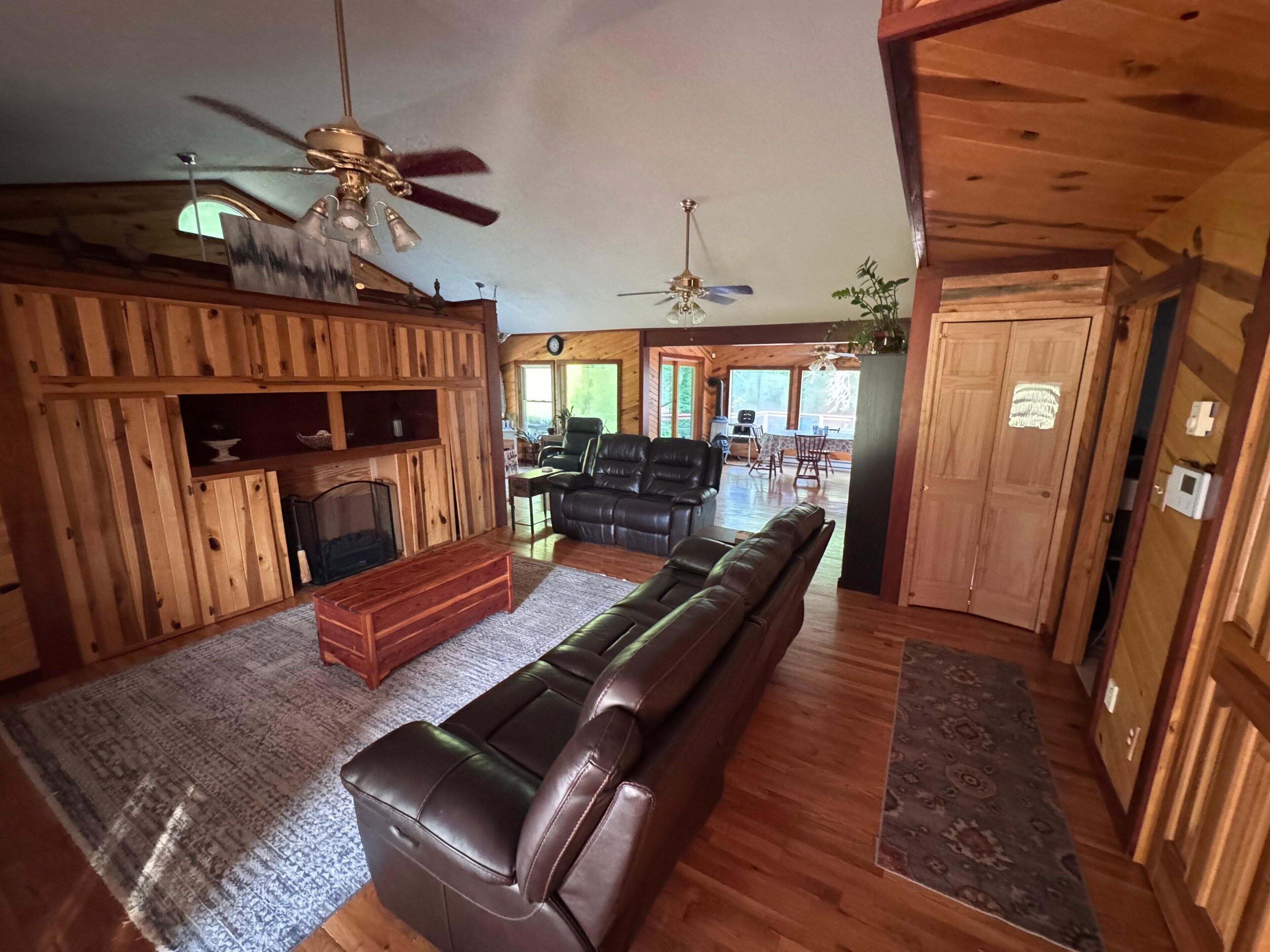 A log cabin interior with a fireplace, leather sofa, dining area, and wooden walls.
