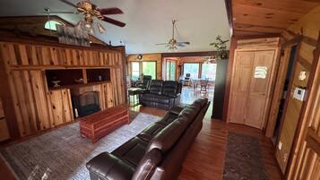 A log cabin interior with a fireplace, leather sofa, dining area, and wooden walls.