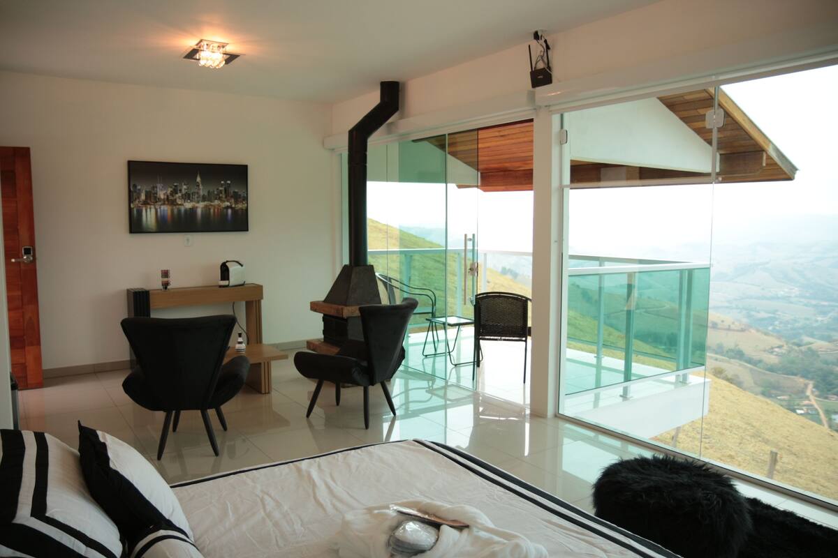Een moderne slaapkamer met een groot bed, een bureau en een stoel. Er is een balkon met een glazen balustrade en uitzicht over het landschap.