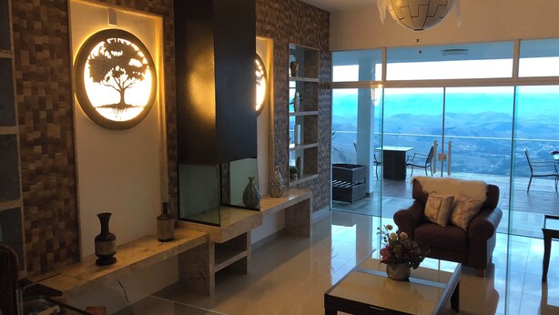 A modern living room with a large mirror, a fireplace, and a view of the mountains through large windows. - Unique Alta Vista Pousada Boutique (Córrego do Bom Jesus)