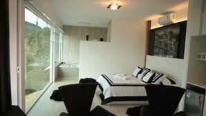 A modern hotel room with a large bed, two black chairs, a small table, and a view of greenery through the window. - Unique Alta Vista Pousada Boutique (Córrego do Bom Jesus)
