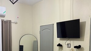 A hotel room with a bed, a TV mounted on the wall, a mirror, and a door.