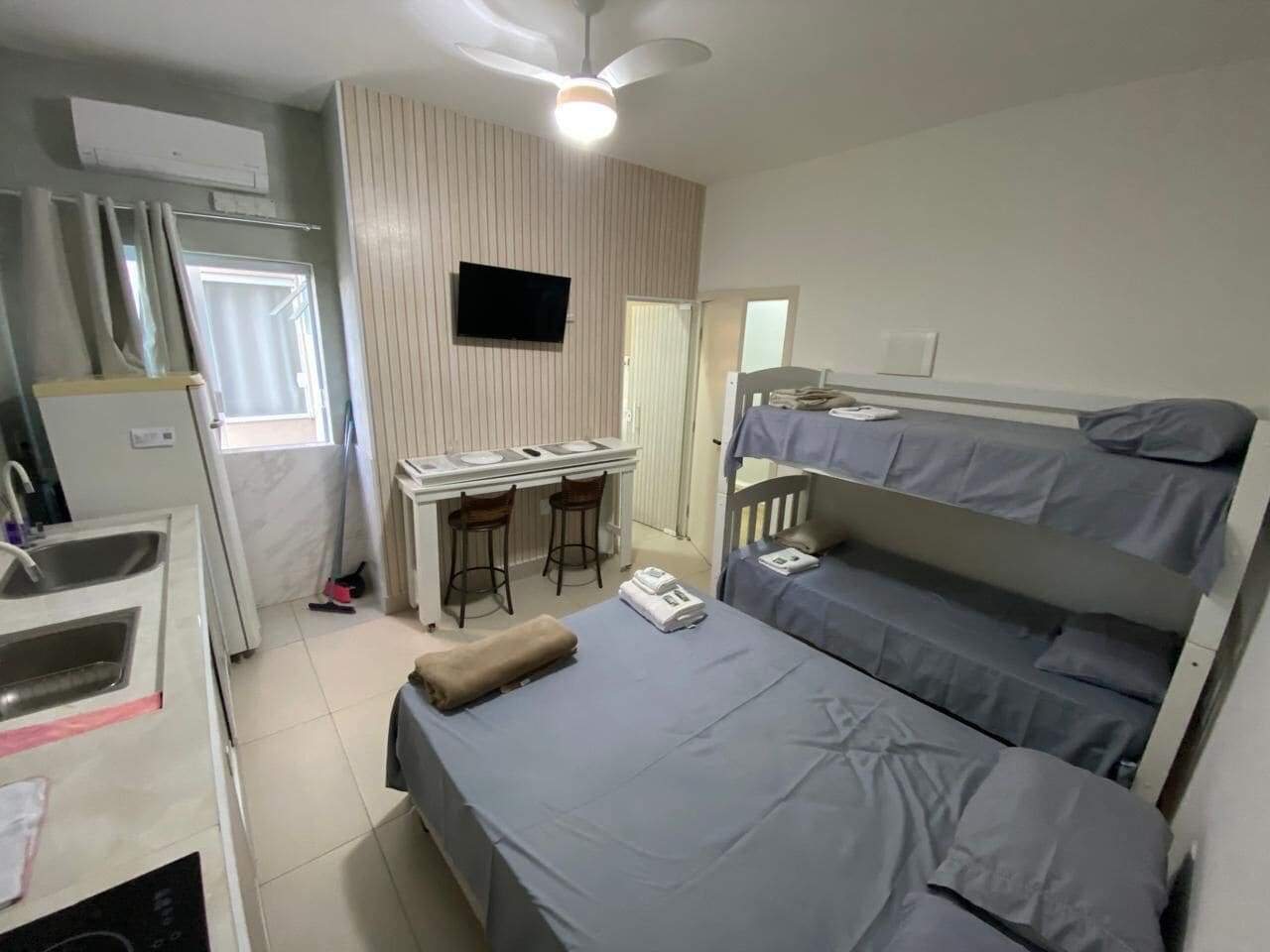 A compact hotel room with a kitchenette, a desk with two chairs, a bunk bed, and a ceiling fan.