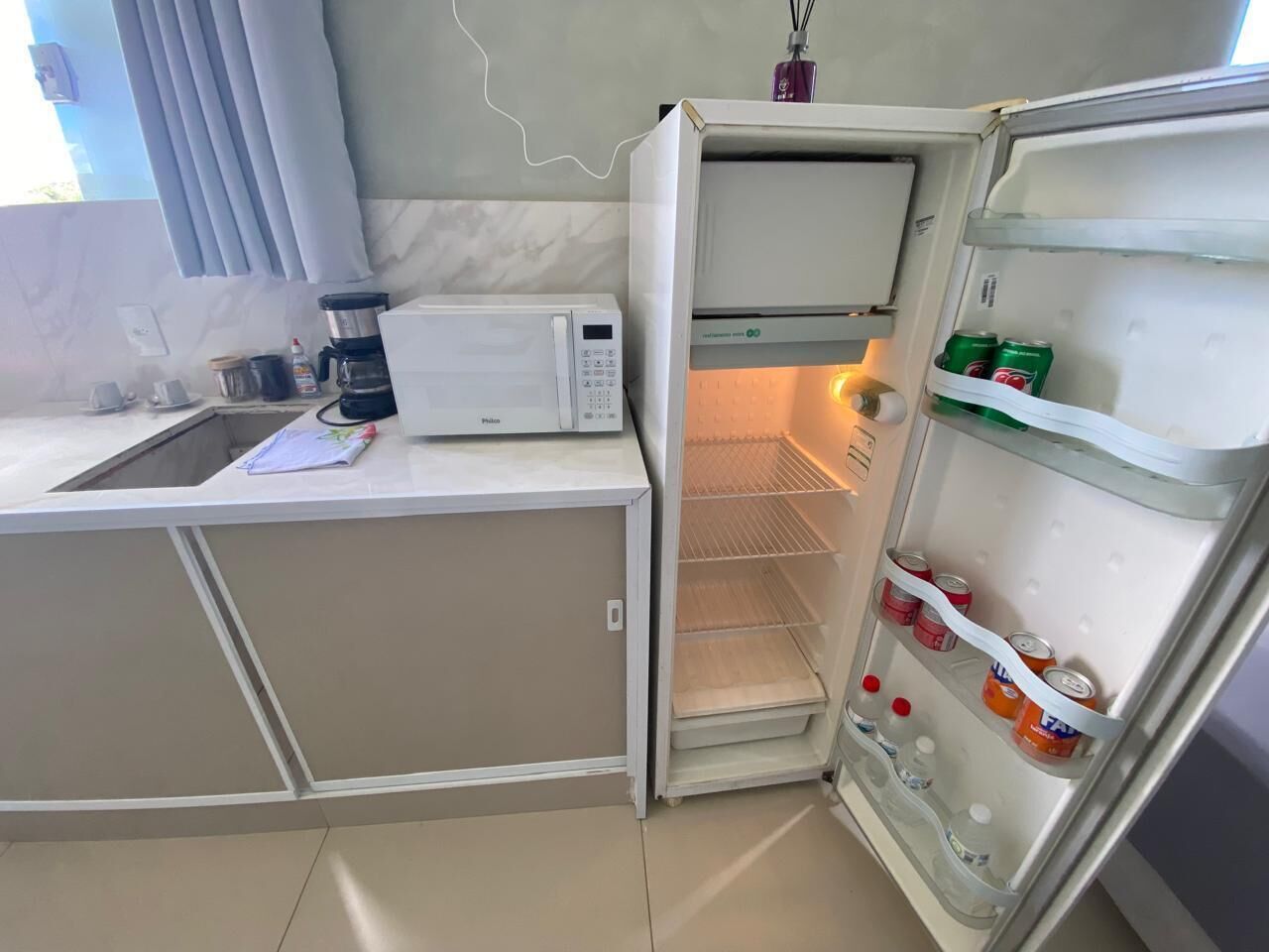 Una cocina compacta equipada con microondas, cafetera y refrigerador lleno de bebidas.