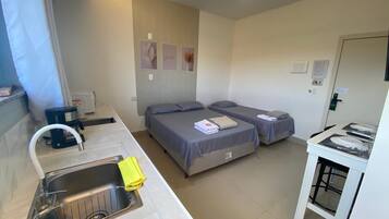 A compact hotel room with a kitchenette, two beds, a ceiling fan, and a small dining area.