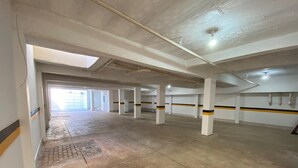 A spacious indoor parking area with concrete floors and white pillars, featuring a skylight and a visible exit. - Hotel Araujo's Suítes (Passos)