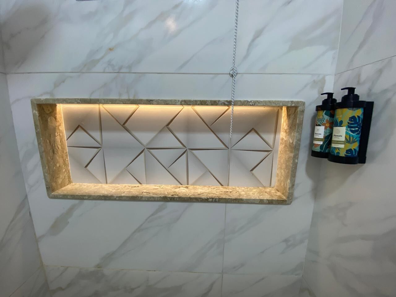 Un baño con pared de mármol, una lámpara de diseño geométrico y dos botellas de champú.