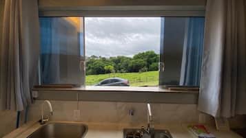 Una cocina con dos fregaderos, una ventana con cortinas y vistas a un coche y vegetación al exterior.