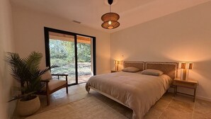 Un dormitorio con una cama grande, un banco, una planta en maceta y vistas al exterior.