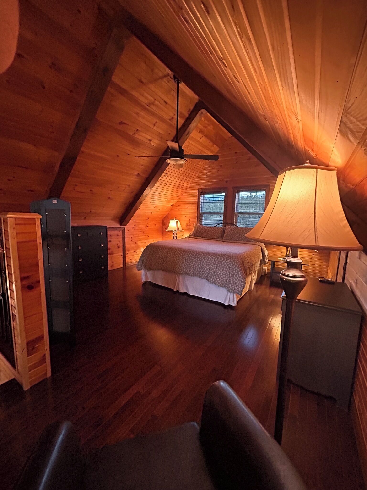 Un dormitorio acogedor en el ático, con techo inclinado, cama, mesita de noche, lámpara y cómoda.