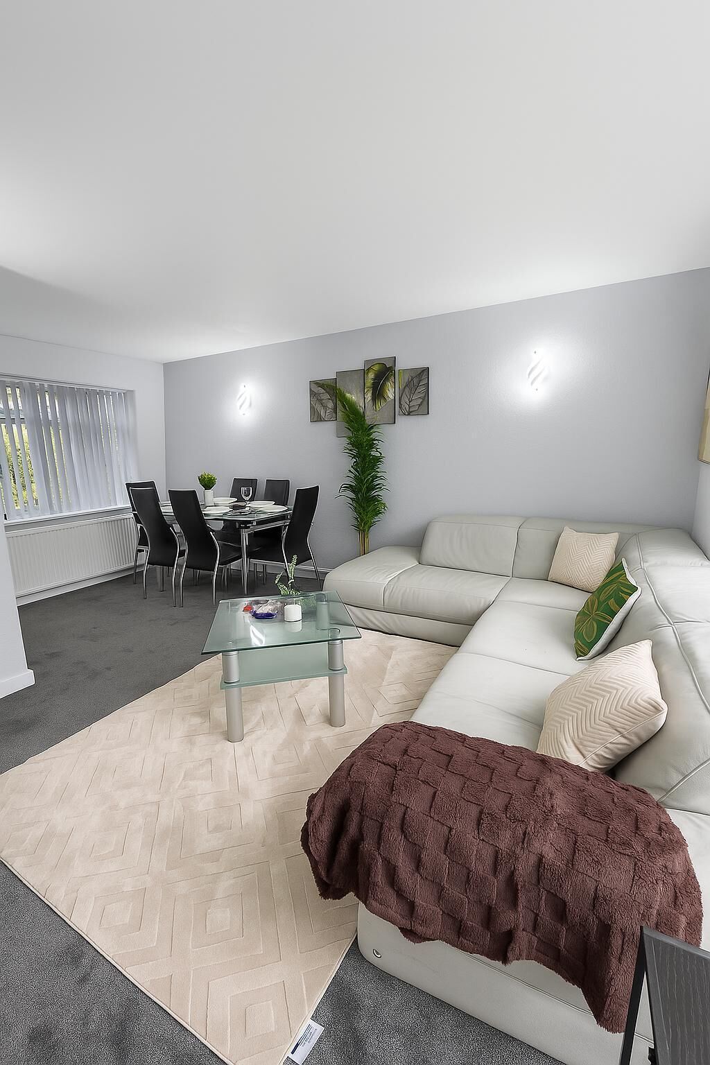 Een moderne woonkamer met een glazen salontafel, een beige bank en een eetgedeelte met een witte tafel en stoelen.