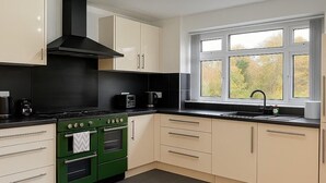 A modern kitchen with a black range hood, a double oven, and a window with a view of trees. - Charming 3BR Sleeps 7 Contractor Stay Driveway (Hale Barns)
