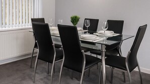 A dining area with a glass table, black chairs, and a small plant centerpiece. - Charming 3BR Sleeps 7 Contractor Stay Driveway (Hale Barns)