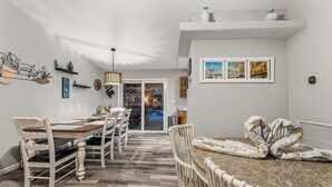 Un comedor con una mesa de madera y sillas blancas, una lámpara colgante y vistas a la cocina.