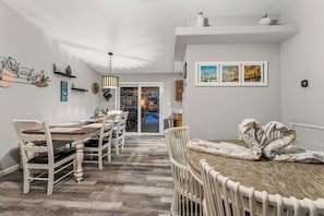 Un comedor con una mesa de madera y sillas blancas, una lámpara colgante y vistas a la cocina.