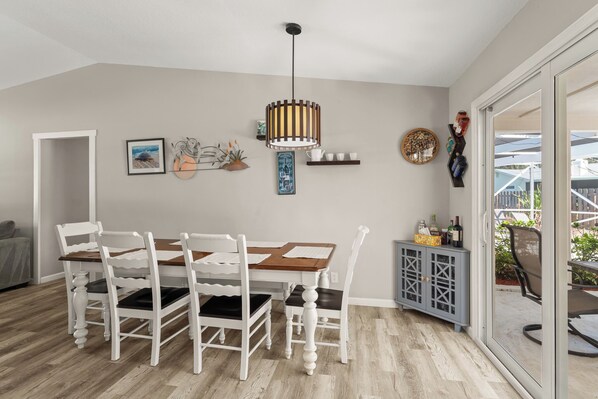Een eetgedeelte met een houten tafel en witte stoelen, een hanglamp en een uitzicht door een glazen deur op een terras.