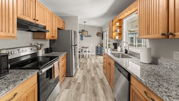 Una cocina moderna con armarios de madera, encimeras de granito y electrodomésticos de acero inoxidable, además de una isla central.