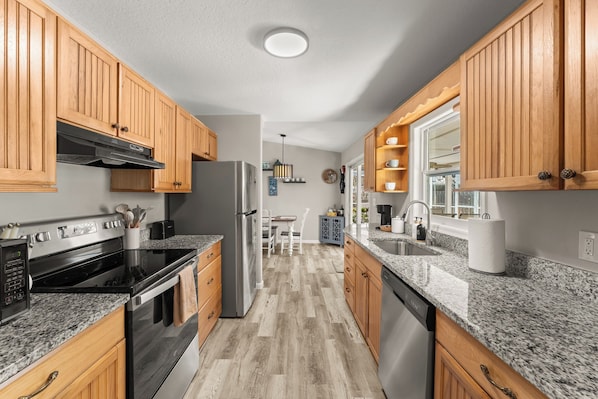 Una cocina moderna con armarios de madera, encimeras de granito y electrodomésticos de acero inoxidable, además de una isla central.