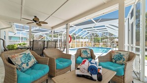 Un espacio de estar al aire libre techado con mobiliario de mimbre, una piscina y un ventilador de techo.