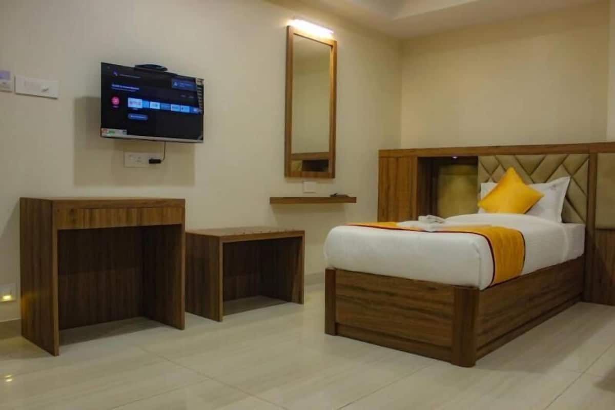 Ein Hotelzimmer mit einem Bett, einem an der Wand befestigten Fernseher und einem Nachttisch aus Holz.