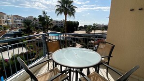 Un balcón con una mesa y sillas de vidrio, con vistas a una piscina y palmeras.