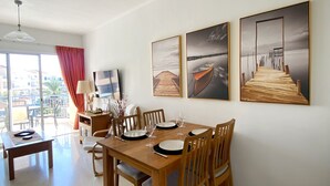 Un comedor con una mesa de madera dispuesta para cuatro, un ventilador de techo y tres cuadros en la pared.