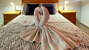 Una cama bien hecha con una toalla doblada en forma de cisne, un cabecero de madera, dos mesitas de noche con lámparas y un cuadro enmarcado en la pared.