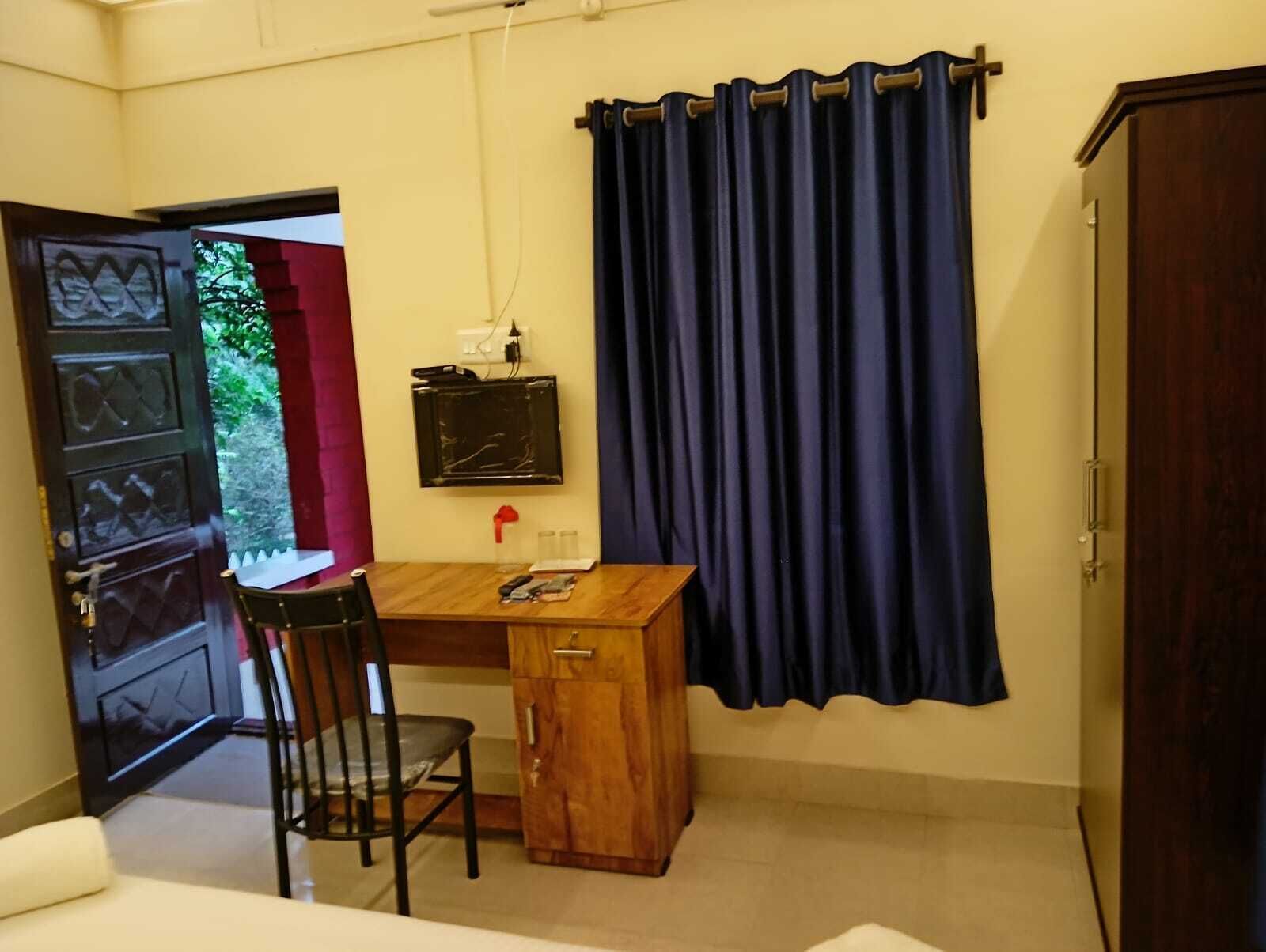 Una habitación pequeña con un escritorio de madera, una silla, un televisor montado en la pared y una cortina oscura.