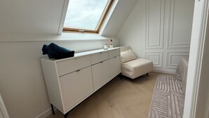 Une pièce avec un plafond en pente, un meuble blanc, un canapé beige et un tapis à motifs.