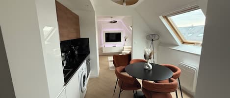 Une cuisine moderne avec un plan de travail noir, un lave-linge et un coin repas comprenant une table ronde et deux chaises.