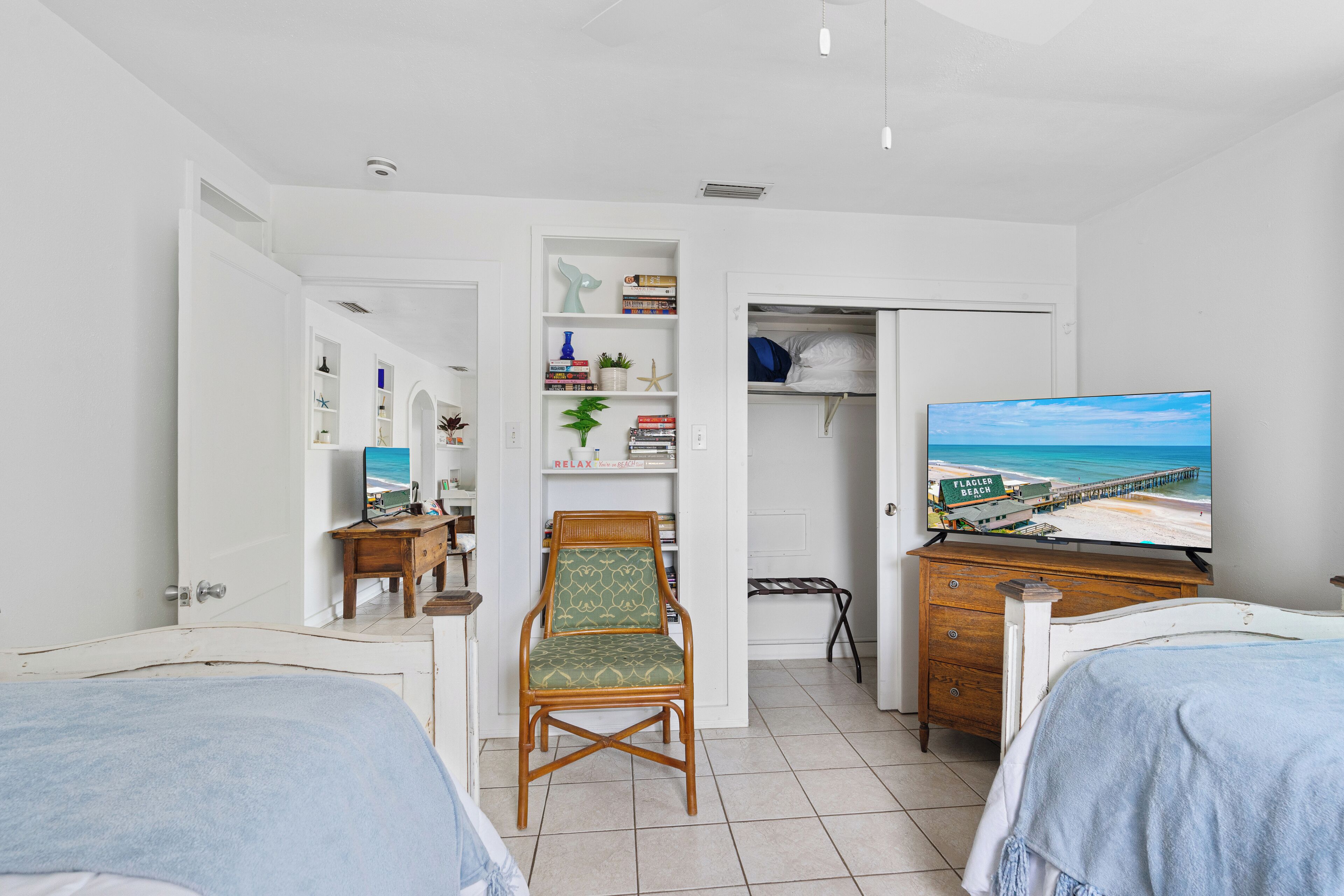 A bedroom with two beds, a chair, a TV, and a wardrobe.