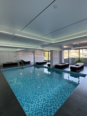Una piscina interna moderna con piastrelle a scacchiera, circondata da aree relax con sedute e vista sull'esterno.