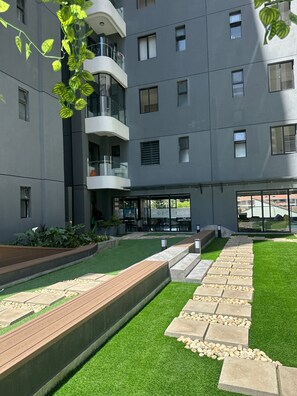 Ein modernes Gebäude mit Innenhof, der künstliches Gras, eine Holzterrasse und eine Sitzgruppe aufweist.