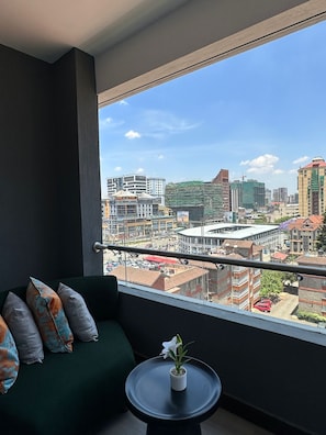 En balkon med udsigt over bybilledet, en grøn sofa og et lille bord med en plante.