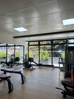 A gym with exercise equipment, large windows, and a view of buildings and greenery. - Perfect 1-bedroom apartment in cool Nairobi with fitness room (Nairobi)