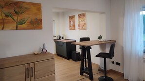A modern kitchen with a wooden table, two bar stools, and a coffee machine. There are two wall-mounted signs indicating coffee and tea options. - Vacation home Franzi with barbecue, garden and terrace, quiet location on the outskirts up to 6 pers (Grebenhain)