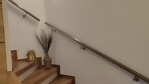 A wooden staircase with a metal handrail and a wall-mounted light fixture. - Vacation home Franzi with barbecue, garden and terrace, quiet location on the outskirts up to 6 pers (Grebenhain)