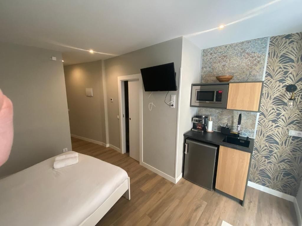 A compact room with a bed, a kitchenette, a TV, and a door leading to another room.